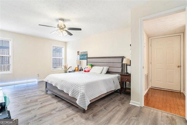 bedroom featuring a ceiling fan, a textured ceiling, baseboards, and wood finished floors