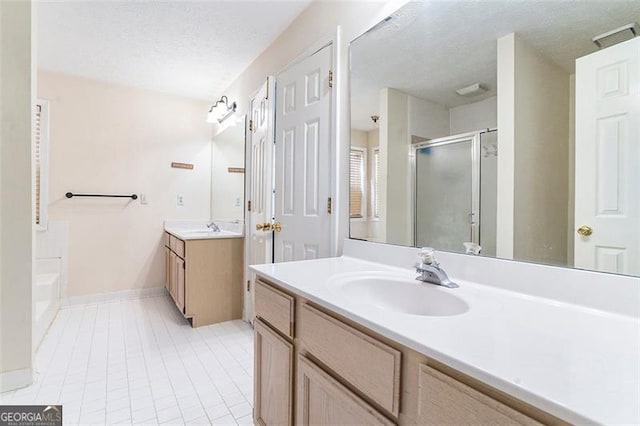 bathroom with a textured ceiling, two vanities, a sink, tile patterned floors, and a stall shower