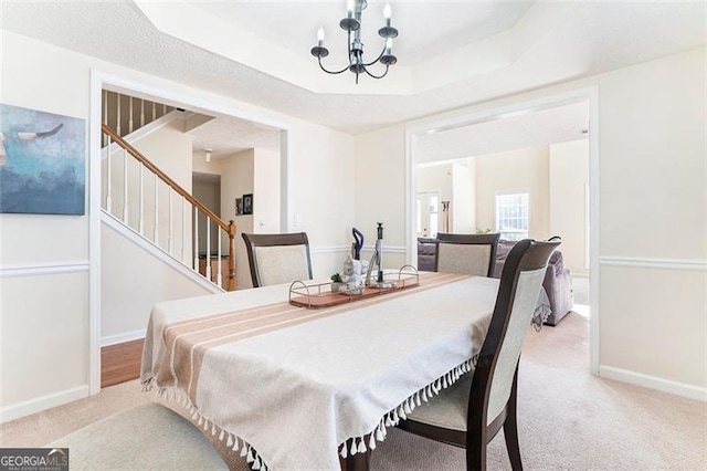 dining area featuring carpet floors, baseboards, stairway, a tray ceiling, and an inviting chandelier