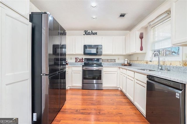 kitchen featuring visible vents, appliances with stainless steel finishes, white cabinets, a sink, and wood finished floors