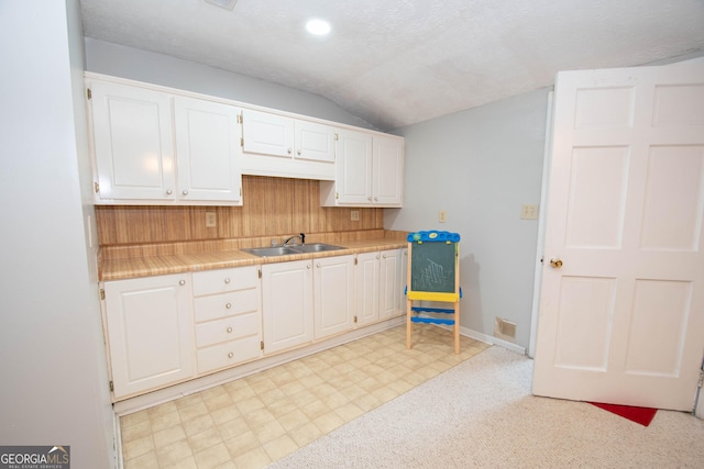 kitchen with visible vents, tile counters, vaulted ceiling, white cabinetry, and a sink