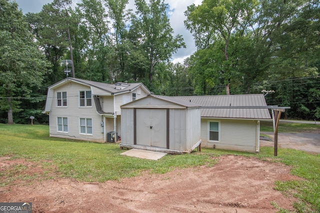 view of front of property featuring central air condition unit, a storage unit, a front yard, metal roof, and an outdoor structure