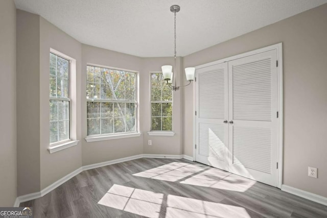 unfurnished dining area featuring a textured ceiling, baseboards, and wood finished floors