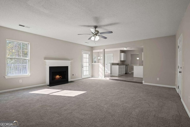 unfurnished living room with baseboards, visible vents, ceiling fan, a fireplace with flush hearth, and carpet flooring