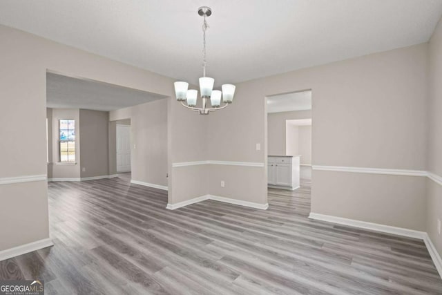 empty room with a chandelier, baseboards, and wood finished floors