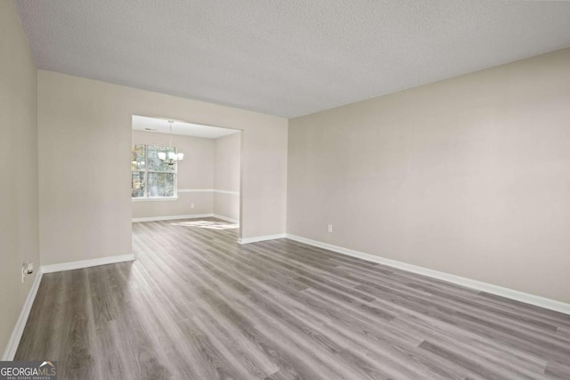 unfurnished room featuring baseboards, a textured ceiling, wood finished floors, and a notable chandelier