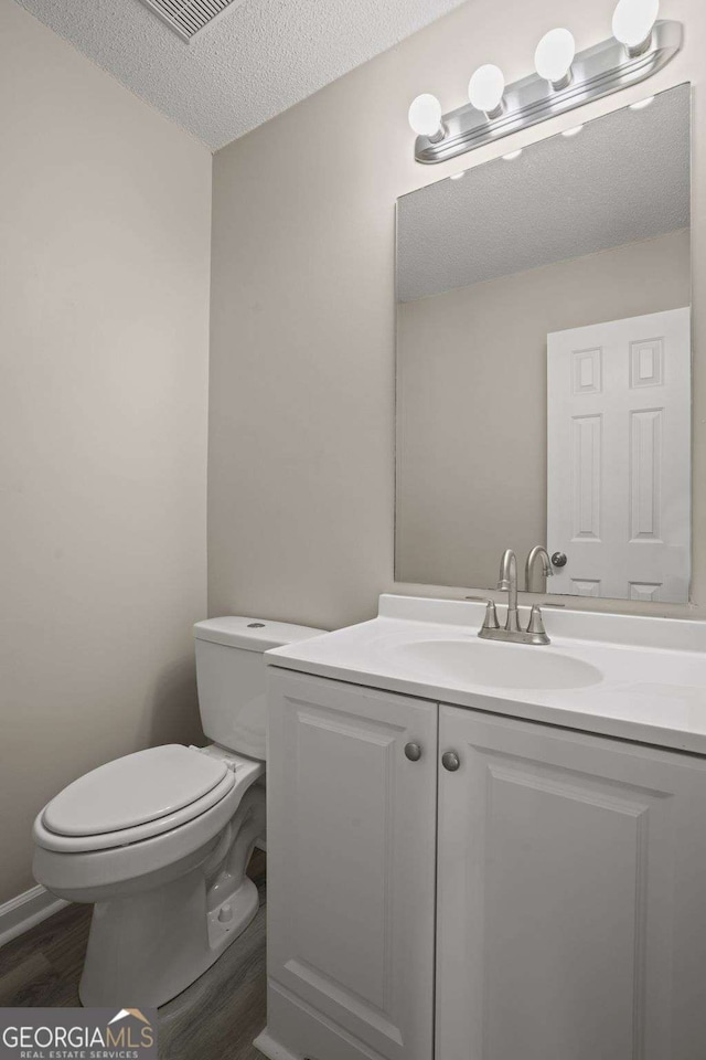 bathroom with a textured ceiling, wood finished floors, vanity, and toilet