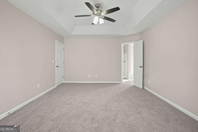 carpeted empty room with a tray ceiling, ceiling fan, and baseboards