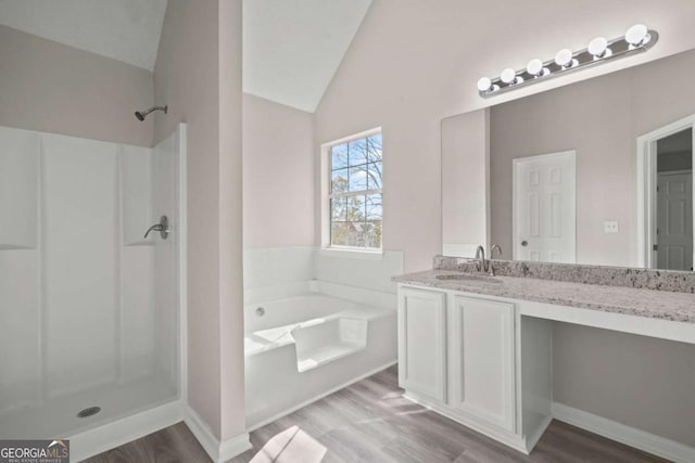 bathroom featuring lofted ceiling, a garden tub, wood finished floors, vanity, and a stall shower