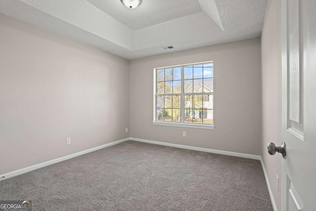 carpeted spare room with a textured ceiling, a tray ceiling, visible vents, and baseboards