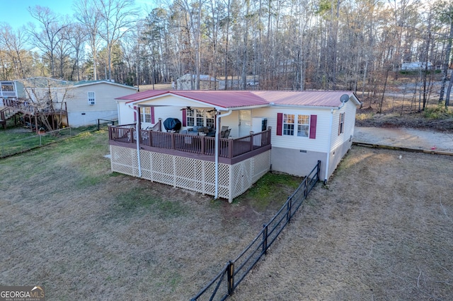 view of front facade with metal roof, fence, driveway, a wooden deck, and a front yard