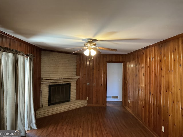 unfurnished living room with wooden walls, visible vents, ceiling fan, wood finished floors, and a brick fireplace