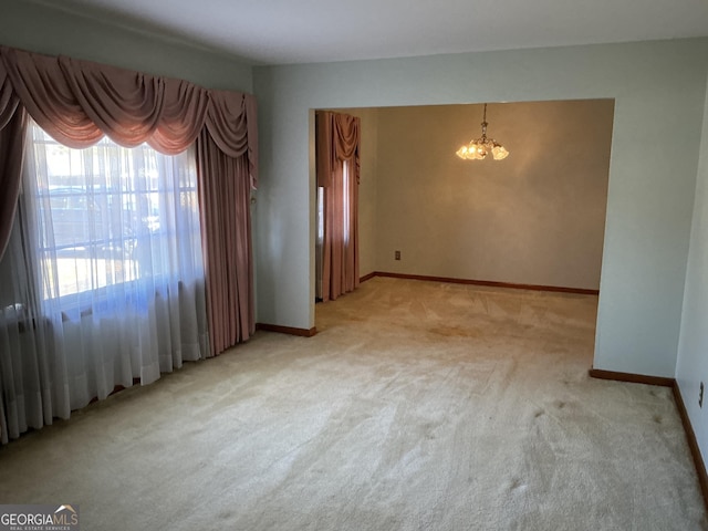 unfurnished room featuring a chandelier, light colored carpet, and baseboards