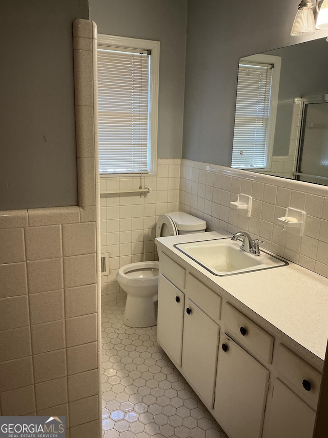 bathroom with toilet, tile walls, vanity, tile patterned floors, and a stall shower