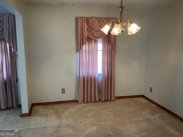 spare room featuring carpet floors, an inviting chandelier, and baseboards