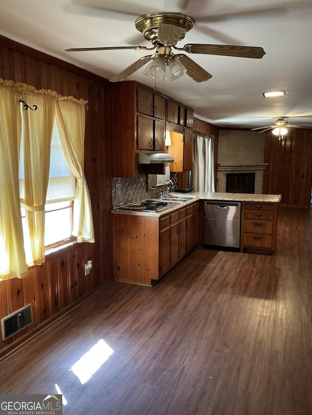 kitchen with visible vents, dark wood finished floors, dishwasher, wood walls, and a sink