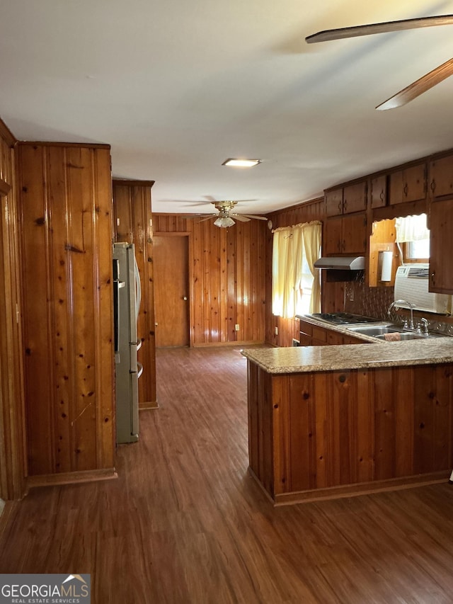 kitchen with brown cabinetry, freestanding refrigerator, ceiling fan, wood finished floors, and under cabinet range hood