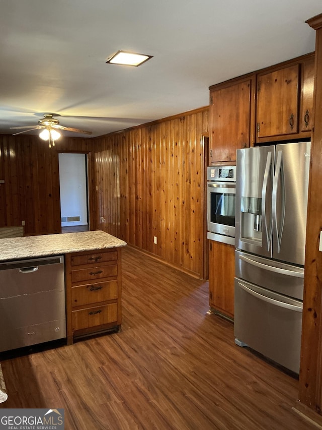 kitchen featuring a ceiling fan, appliances with stainless steel finishes, brown cabinets, and dark wood finished floors