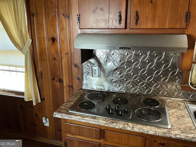 kitchen with brown cabinets, stainless steel electric stovetop, and wall chimney exhaust hood