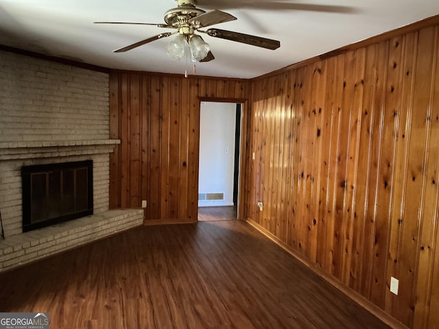 unfurnished living room featuring a fireplace, visible vents, wooden walls, wood finished floors, and baseboards