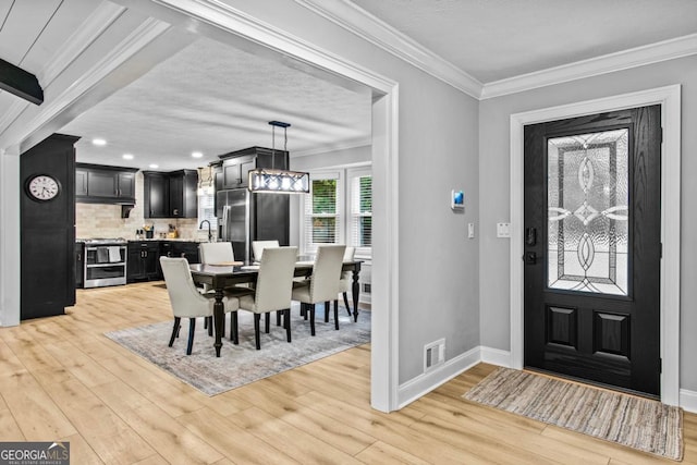 entrance foyer featuring visible vents, ornamental molding, light wood-style floors, a textured ceiling, and baseboards