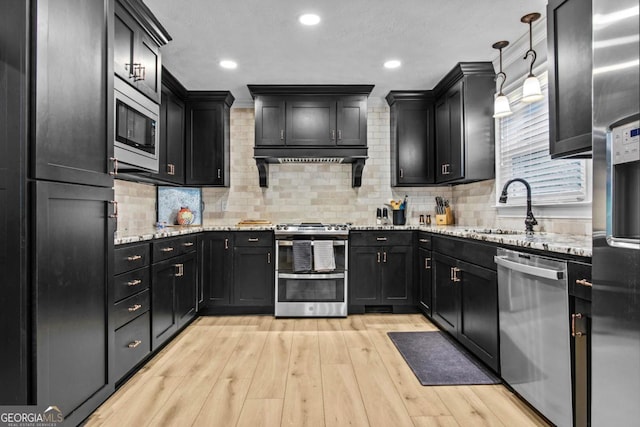 kitchen with light wood finished floors, tasteful backsplash, appliances with stainless steel finishes, light stone counters, and a sink