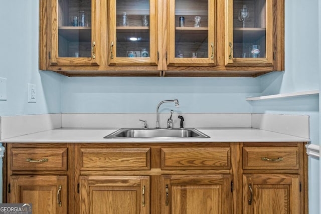 kitchen with light countertops, brown cabinetry, a sink, and glass insert cabinets