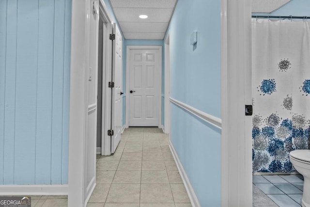 hallway featuring light tile patterned flooring, a paneled ceiling, and baseboards