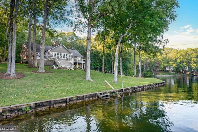 dock area featuring stairway, a deck with water view, and a yard