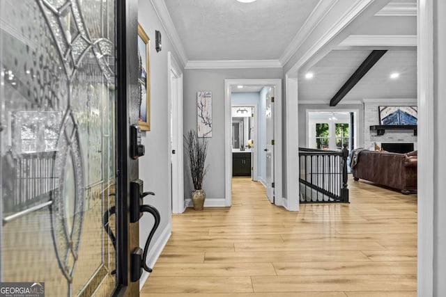 entrance foyer featuring light wood-style floors, a textured ceiling, ornamental molding, and beamed ceiling