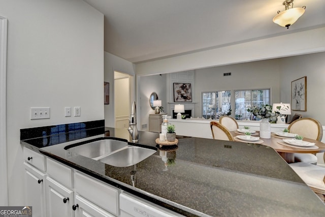 kitchen featuring visible vents, open floor plan, white cabinetry, a sink, and dark stone counters