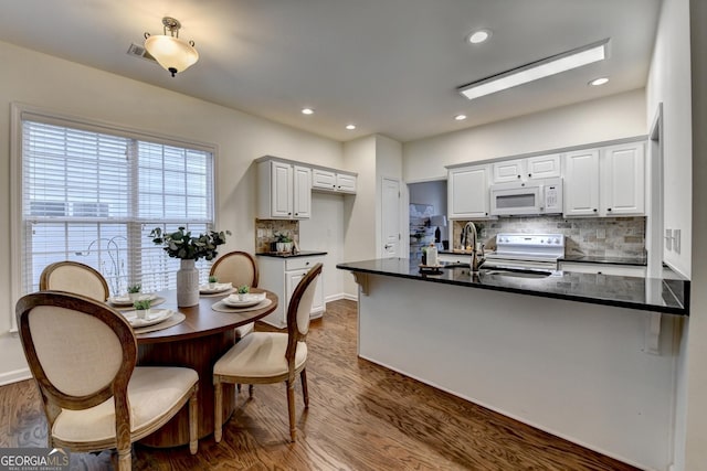 kitchen featuring dark wood finished floors, dark countertops, white microwave, range with electric cooktop, and a peninsula