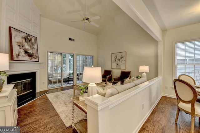 living area featuring visible vents, a ceiling fan, dark wood-type flooring, a fireplace, and high vaulted ceiling