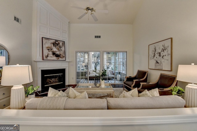 living area with a high ceiling, ceiling fan, a fireplace, and visible vents