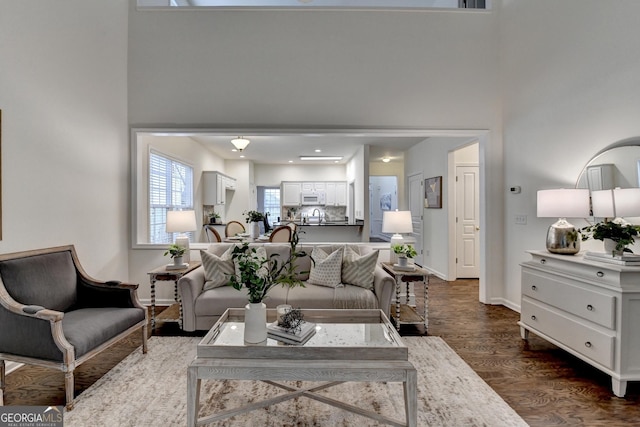 living area with dark wood-style flooring, a high ceiling, and baseboards