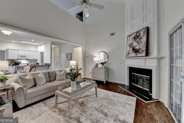 living room with a large fireplace, baseboards, visible vents, a ceiling fan, and dark wood-style flooring