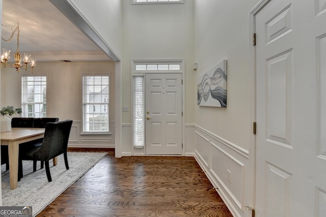 entryway with an inviting chandelier, a decorative wall, dark wood-type flooring, and wainscoting