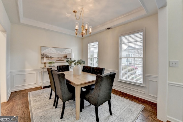 dining area featuring a chandelier, a wainscoted wall, wood finished floors, visible vents, and a raised ceiling