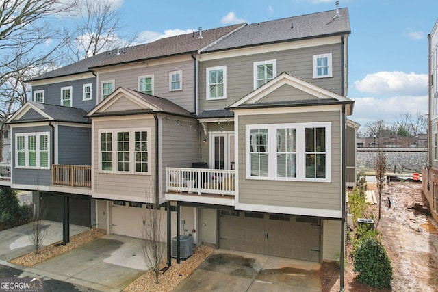 rear view of house with a garage, central AC unit, driveway, and a shingled roof