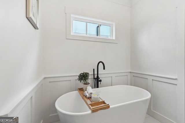 bathroom featuring a decorative wall, wainscoting, and a freestanding bath