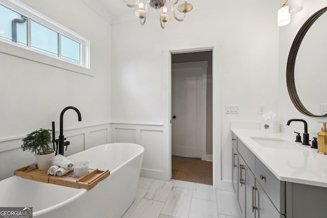 full bath with vanity, a freestanding tub, wainscoting, a decorative wall, and a notable chandelier