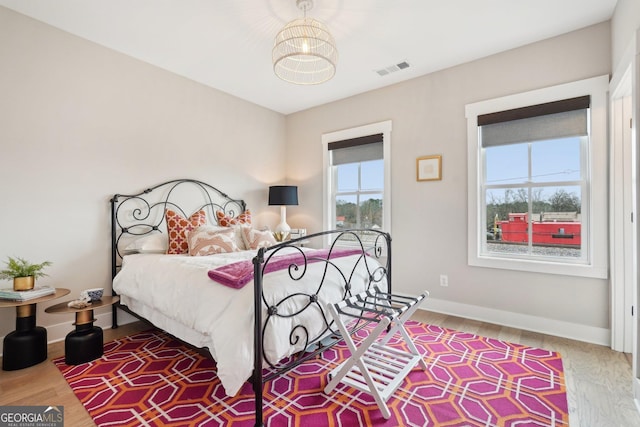 bedroom featuring a chandelier, visible vents, baseboards, and wood finished floors