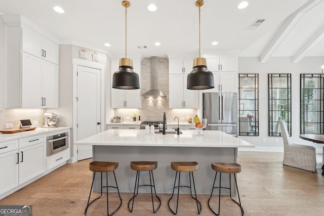 kitchen featuring wall chimney range hood, light wood finished floors, a breakfast bar area, and appliances with stainless steel finishes