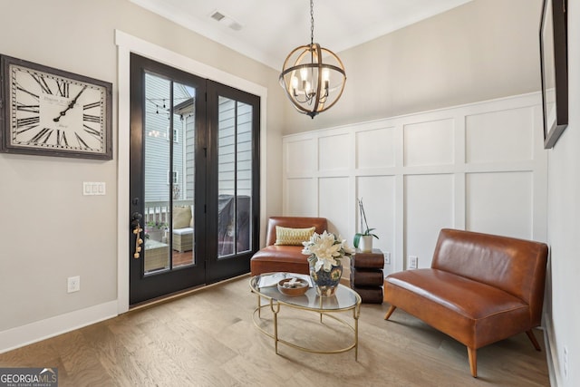 living area featuring an inviting chandelier, a decorative wall, wood finished floors, and visible vents