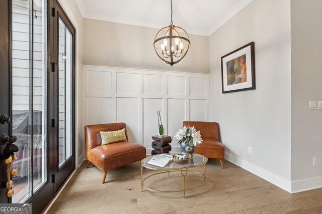 sitting room with wood finished floors, baseboards, an inviting chandelier, crown molding, and a decorative wall
