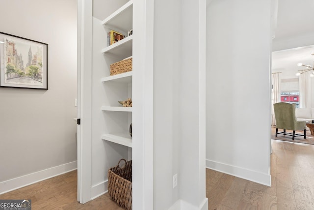 hall with a chandelier, built in shelves, baseboards, and wood finished floors