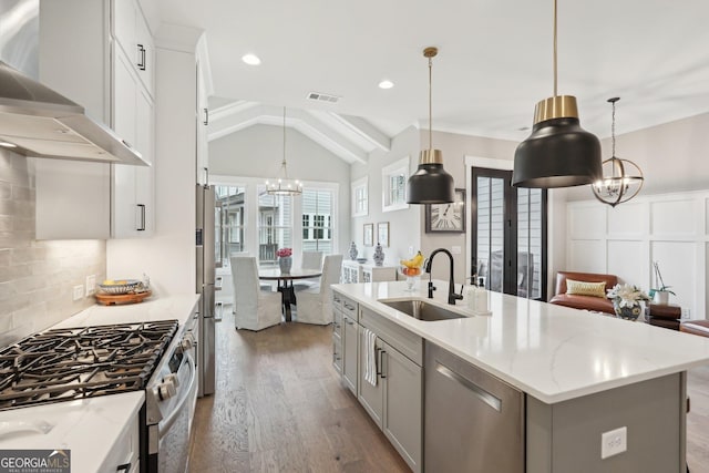 kitchen with visible vents, a chandelier, appliances with stainless steel finishes, wall chimney exhaust hood, and a sink