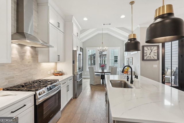 kitchen with visible vents, wall chimney range hood, a chandelier, stainless steel appliances, and a sink