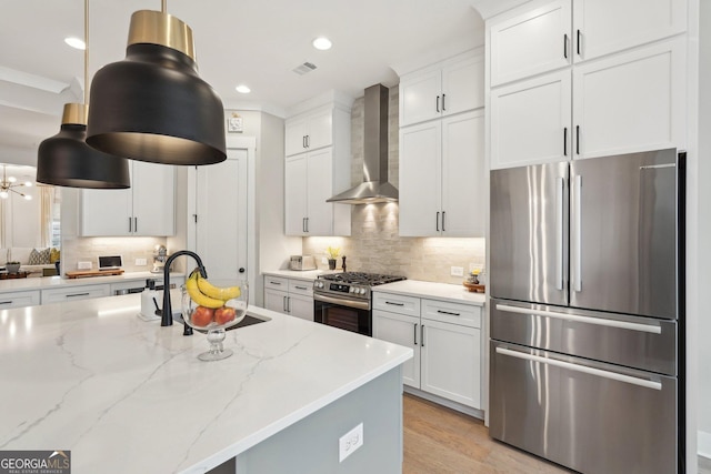 kitchen featuring visible vents, a sink, appliances with stainless steel finishes, wall chimney exhaust hood, and tasteful backsplash