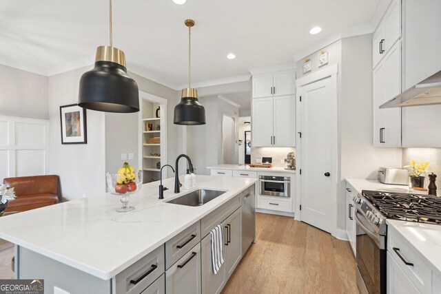 kitchen featuring a center island with sink, stainless steel appliances, a sink, crown molding, and wall chimney range hood